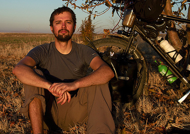 Christian Benke sitting in the grass in an apricot orchard in Turkey, part of his touring bicylce next to him
